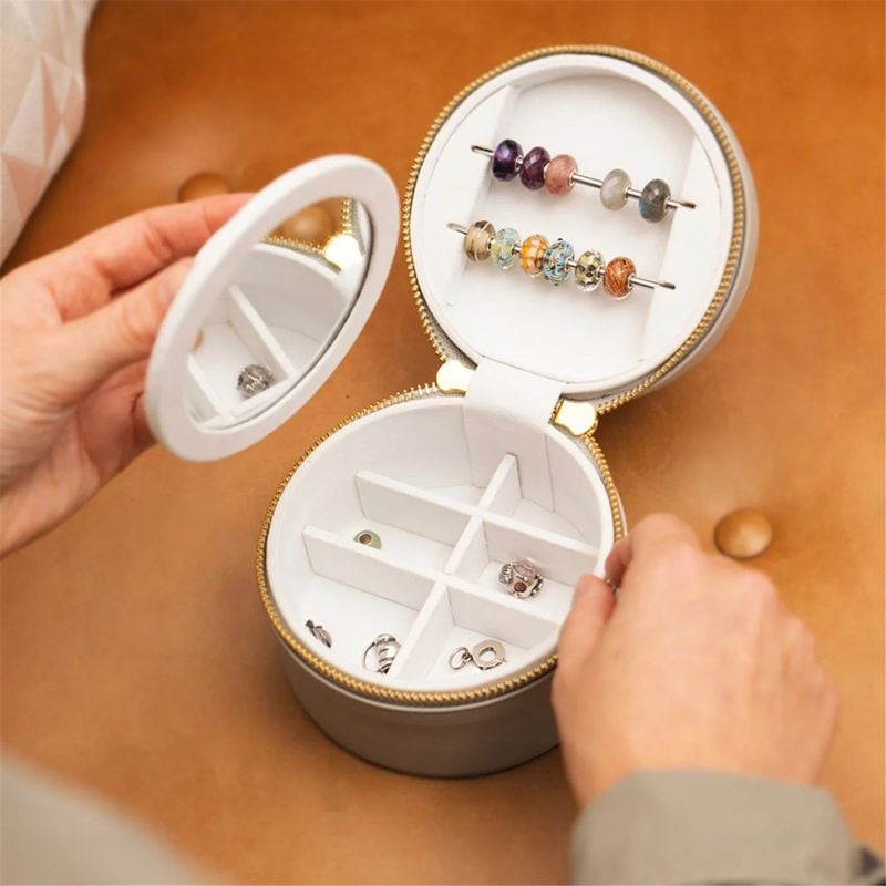 Des mains ouvrent la boîte de voyage Trollbeads crème : perles colorées sur le couvercle et breloque