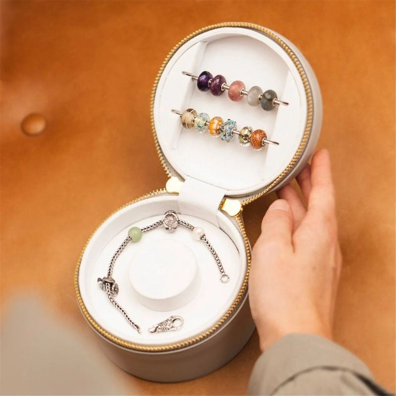 Boîte crème Trollbeads ouverte avec un bracelet argent dans la base et des perles colorées dans le c