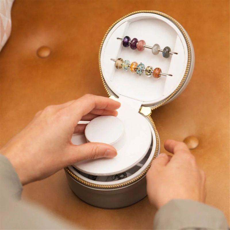 Mains soulevant le plateau amovible d'une boîte à bijoux de voyage Trollbeads crème pleine de perles