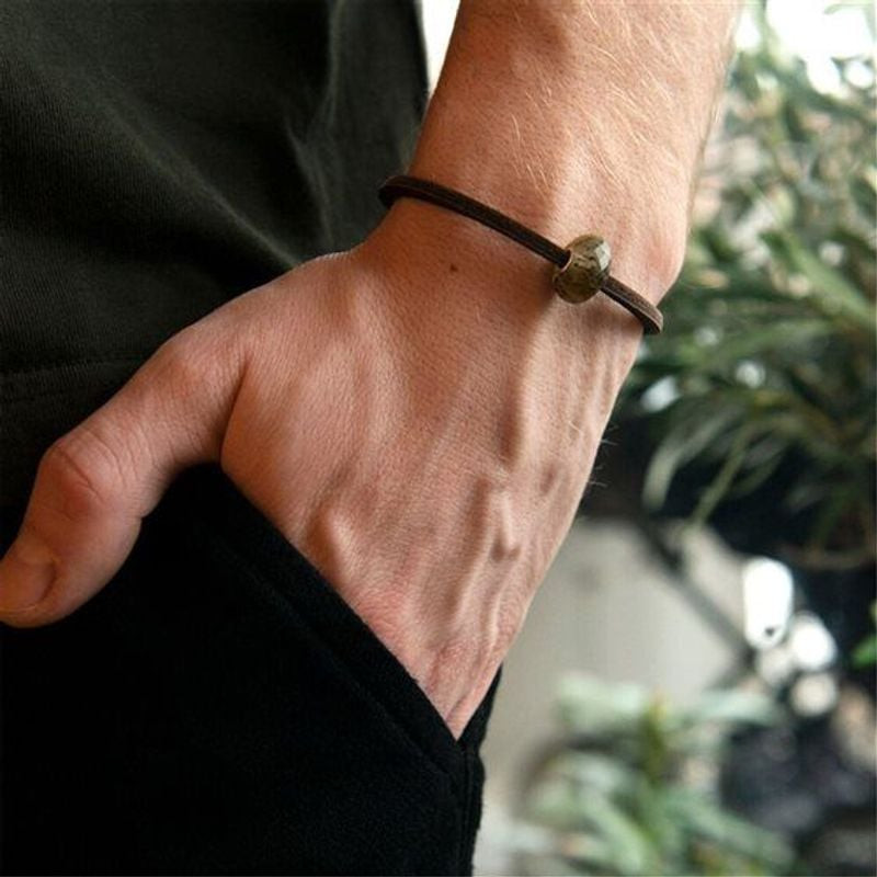 Gros plan d'un poignet portant le bracelet en cuir marron Trollbeads avec un charm, main dans la poc