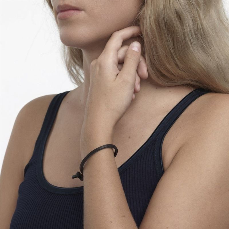 Femme en débardeur noir portant le bracelet Trollbeads simple en cuir noir à son poignet, main levée