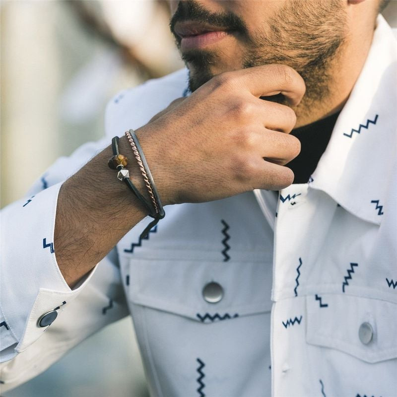Homme en chemise blanche à motifs portant le bracelet Trollbeads en cuir noir avec d'autres bracelet