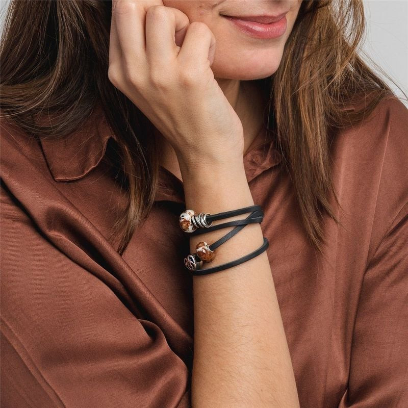 Femme portant un bracelet Trollbeads double tour en cuir noir orné de breloques en verre blanc et cu