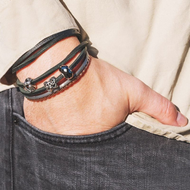 Poignet d'homme portant un bracelet Trollbeads en cuir noir enroulé deux fois avec des breloques et 