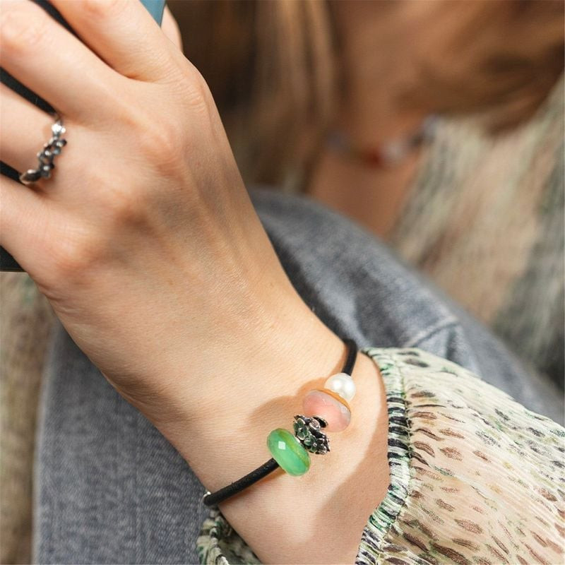 Main portant un bracelet avec la perle TROLLBEADS PIERRE D'EAU SAUGE et d'autres perles colorées.