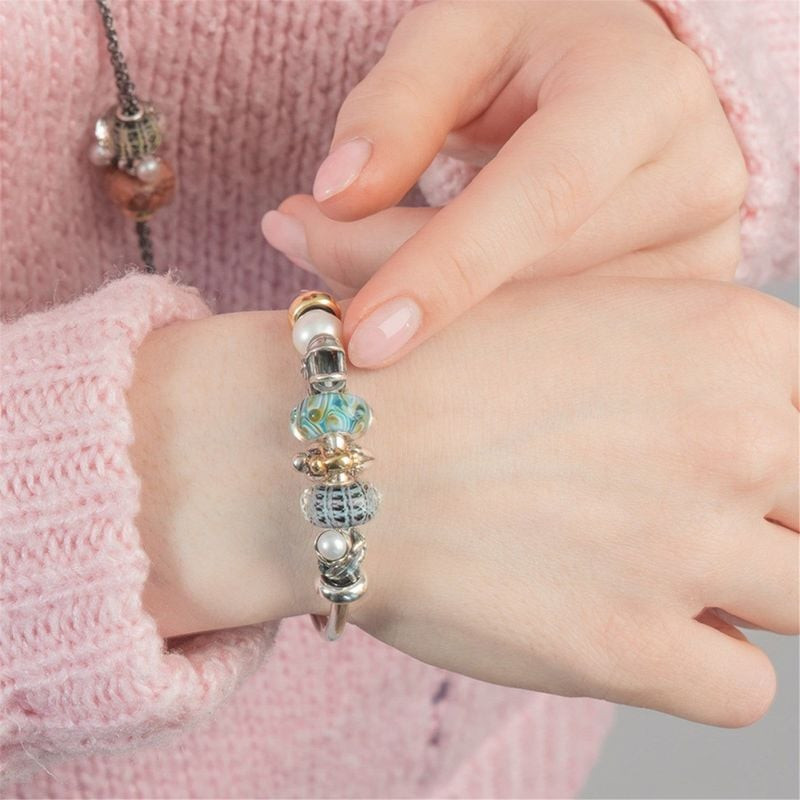Poignet d'une femme portant un jonc Trollbeads avec la perle de verre Panier de la Sérénité et une m