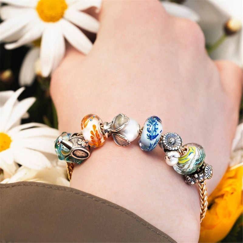 Bracelet Trollbeads avec perles de verre et fleurs bleues, dont la perle Vie Actuelle, porté parmi d