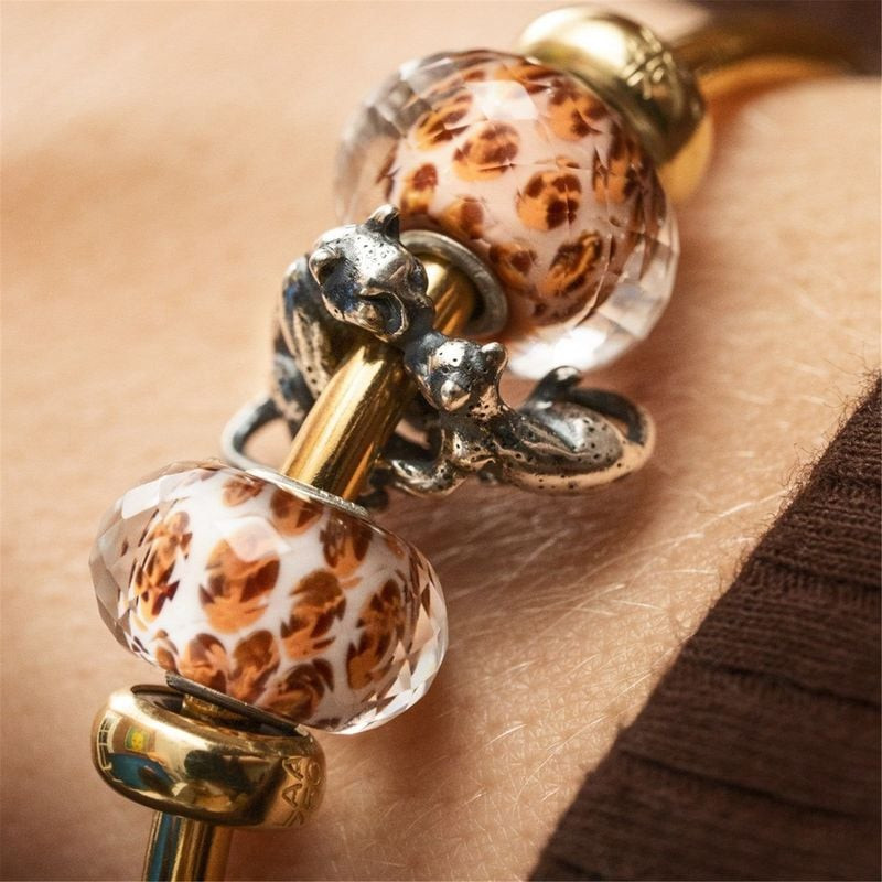Deux perles en verre Trollbeads Taches de Léopard sur bracelet jonc doré, avec charms léopard argent