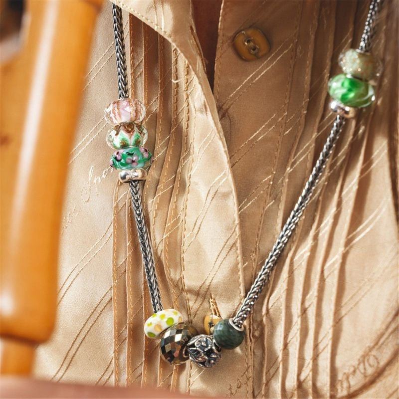 Perles en verre Trollbeads portées sur chaînes argentées avec une blouse en soie beige sous une lumi