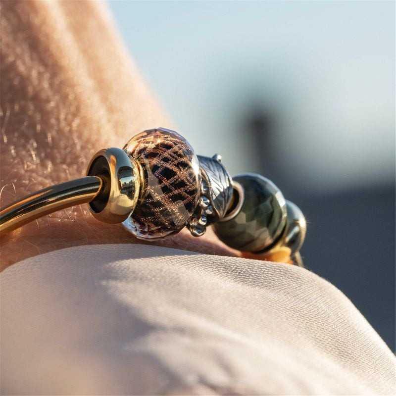 Perle de verre Trollbeads Happy 2023 portée sur un jonc doré au poignet, illuminée par la lumière ch