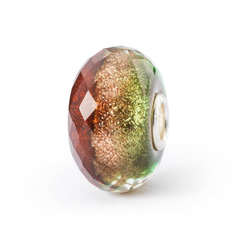 Perle à charms Trollbeads en verre facetté avec des reflets rouge, vert et or sur fond blanc uni