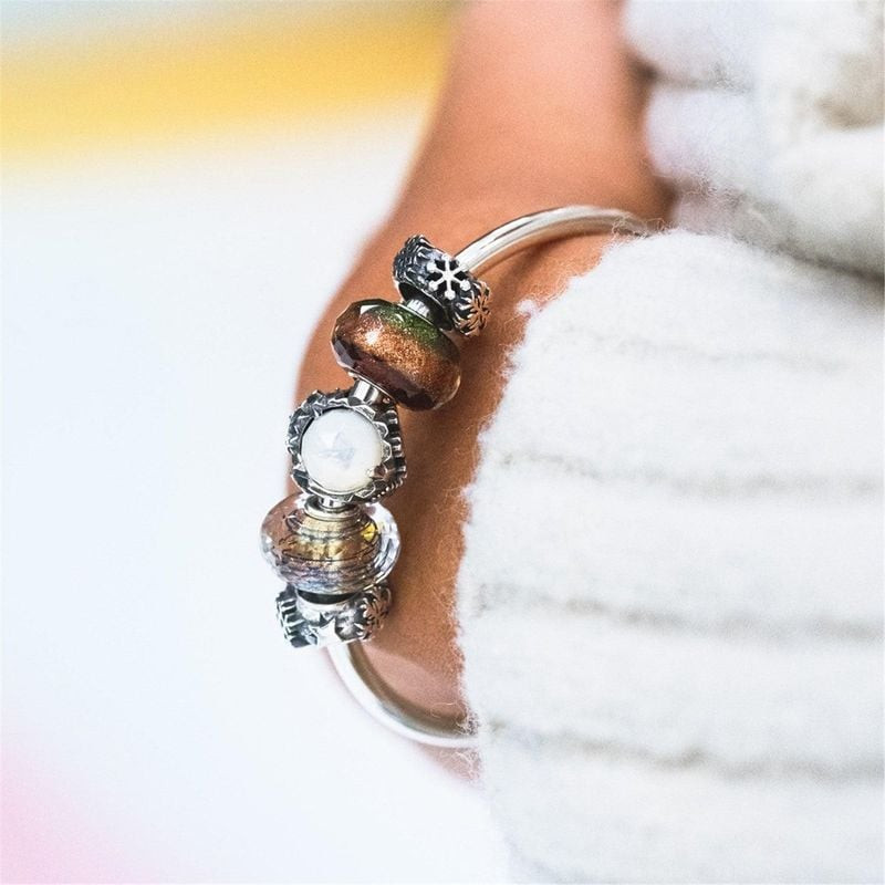 Gros plan d'un bracelet Trollbeads porté au poignet, perle en verre facetté Vœux Chaleureux sur manc