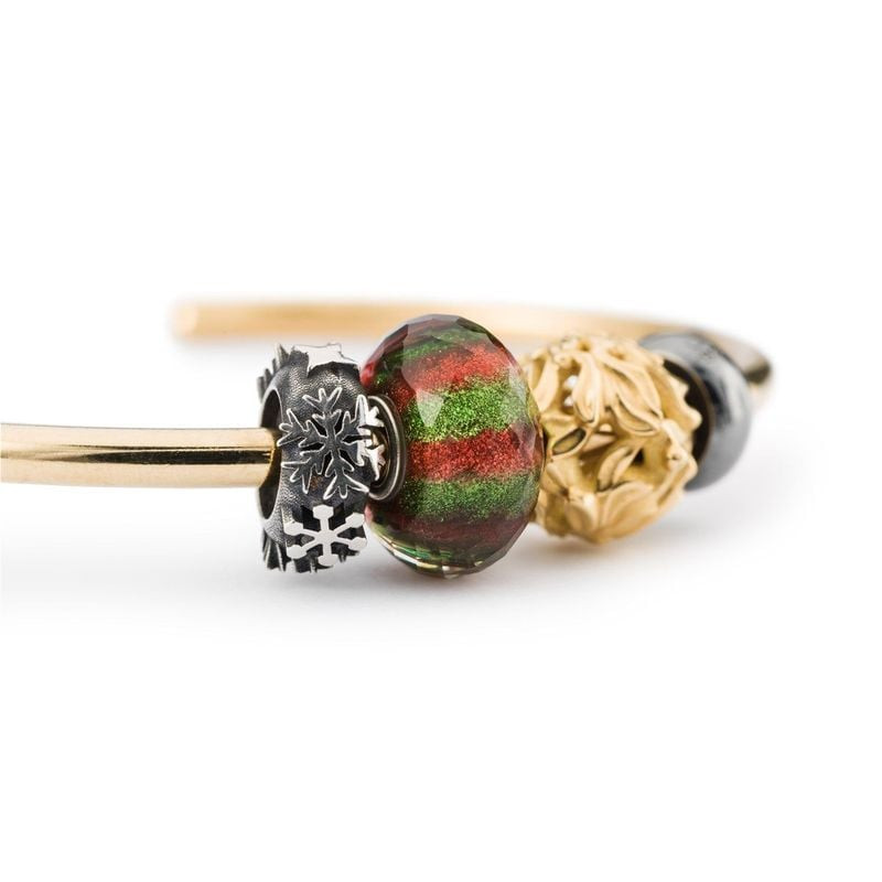 Perle de charme Trollbeads en verre entre des charms feuille d'or et flocon de neige argenté sur fon