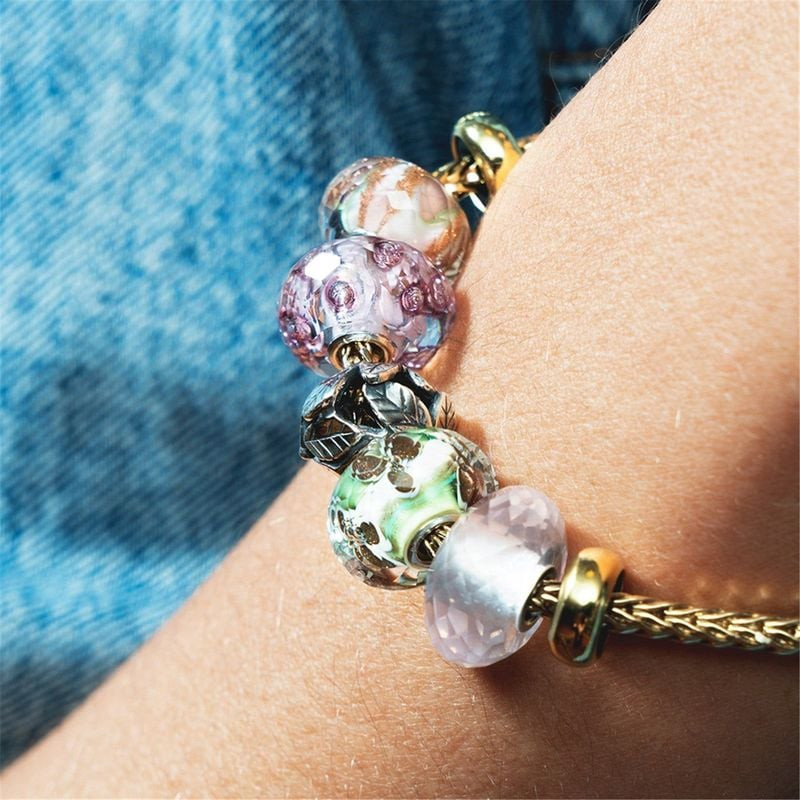 Un bras portant un bracelet Trollbeads doré orné de diverses perles de verre, dont la perle Lit de F