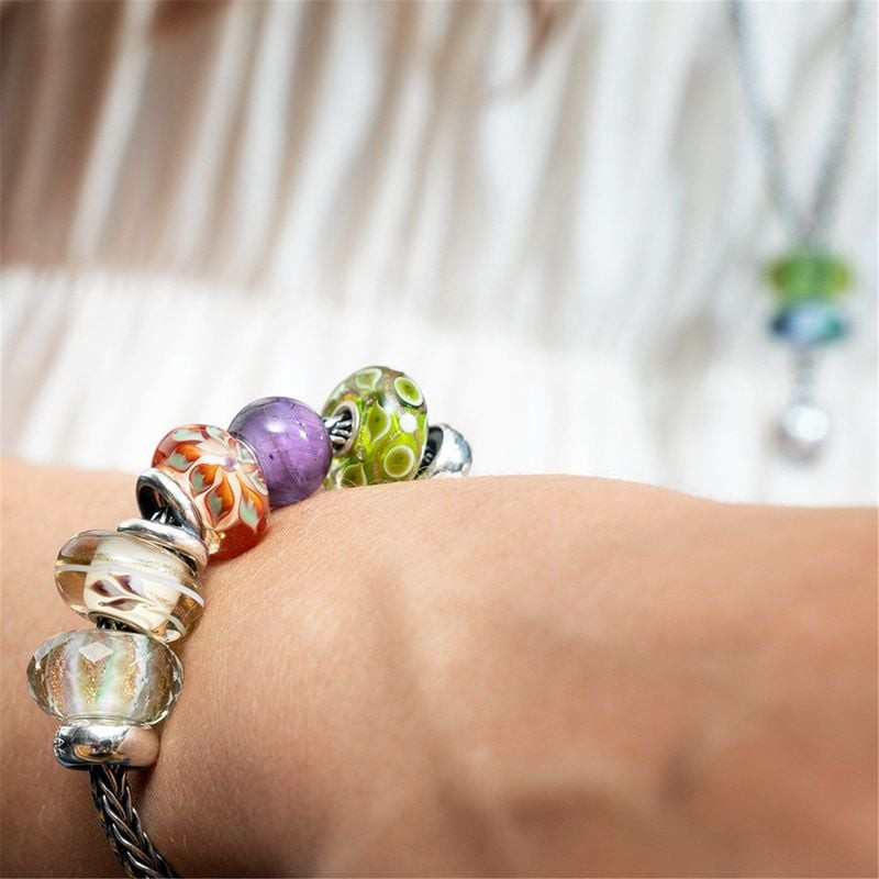 Gros plan d'un bracelet Trollbeads au poignet, avec la perle Lit de Fleurs et d'autres perles de ver