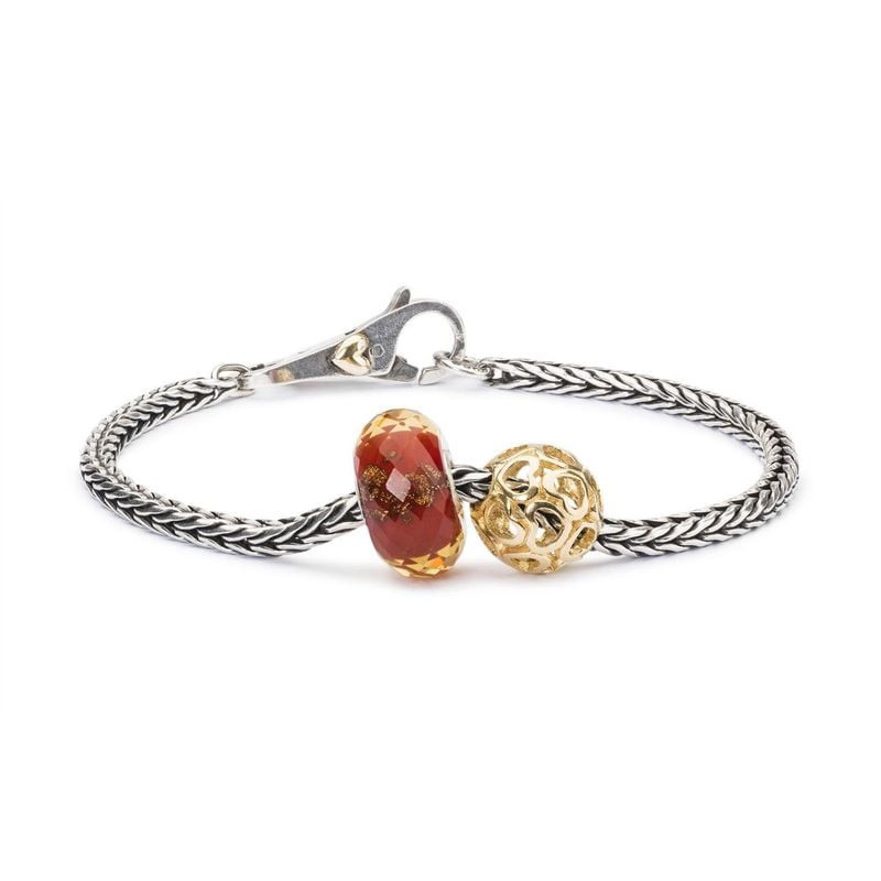 Charm TROLLBEADS en verre rouge à côté d'une perle dorée filigranée sur bracelet argent tressé