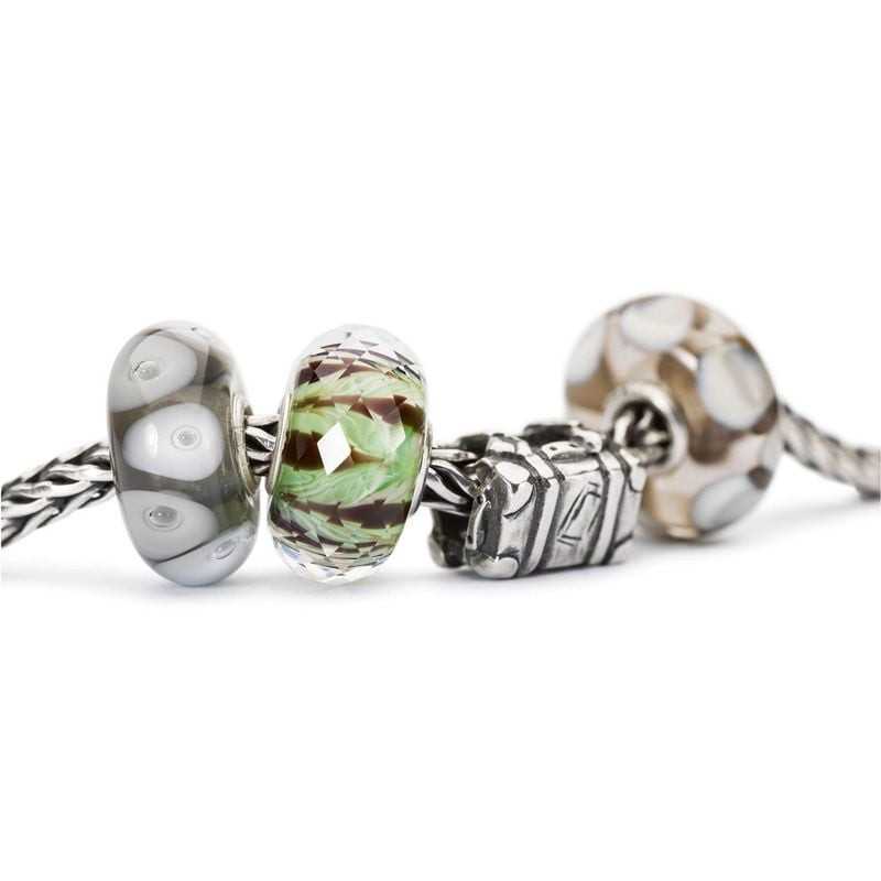 Gros plan sur la perle de charme Trollbeads Jungle en verre facetté aux côtés de charms Trollbeads g