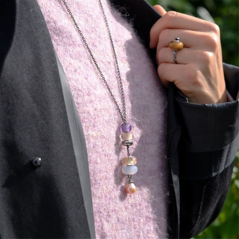 Femme en manteau noir à revers en feutre rose portant un collier Trollbeads avec perles de charme en