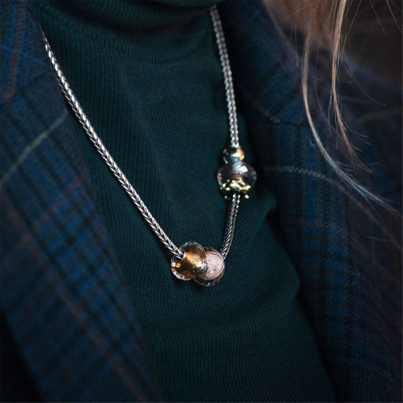 Perles de charme Trollbeads en verre sur collier argent tressé porté sur un pull col roulé vert fonc
