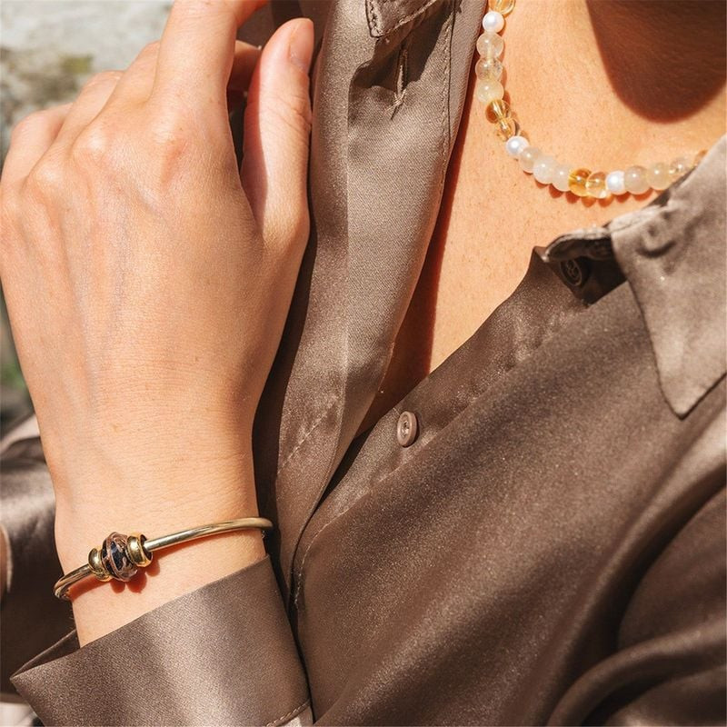 Femme portant un jonc doré Trollbeads avec la perle Branches Dorées et un collier de perles