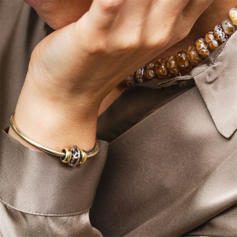 Gros plan d'un poignet portant un jonc Trollbeads doré avec la perle de verre Branches Dorées
