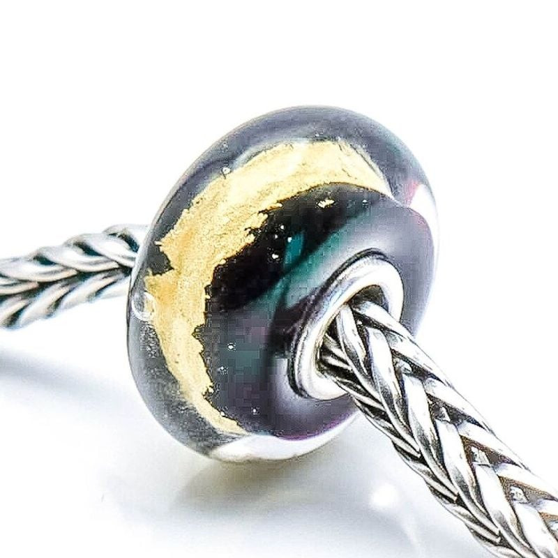 Gros plan de la breloque Trollbeads Or noir en verre sur une chaîne en argent, inclinée pour révéler