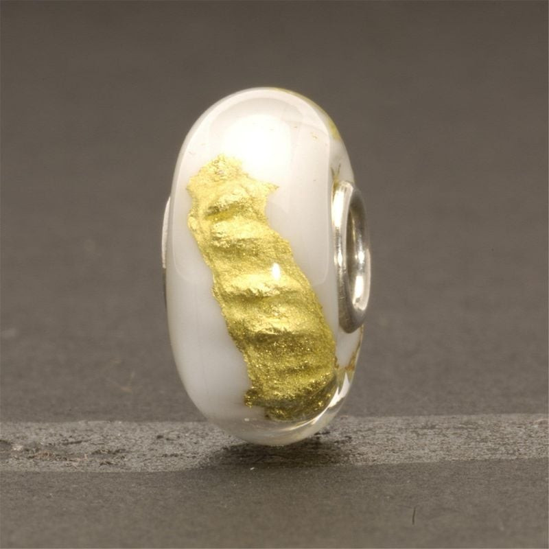 Perle Trollbeads Chakra Couronne posée sur pierre grise, verre blanc et bande dorée scintillante