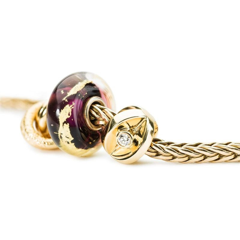 Perle Trollbeads Troisième œil sur chaîne dorée à côté d'une bille d'arrêt dorée sertie d'un cristal