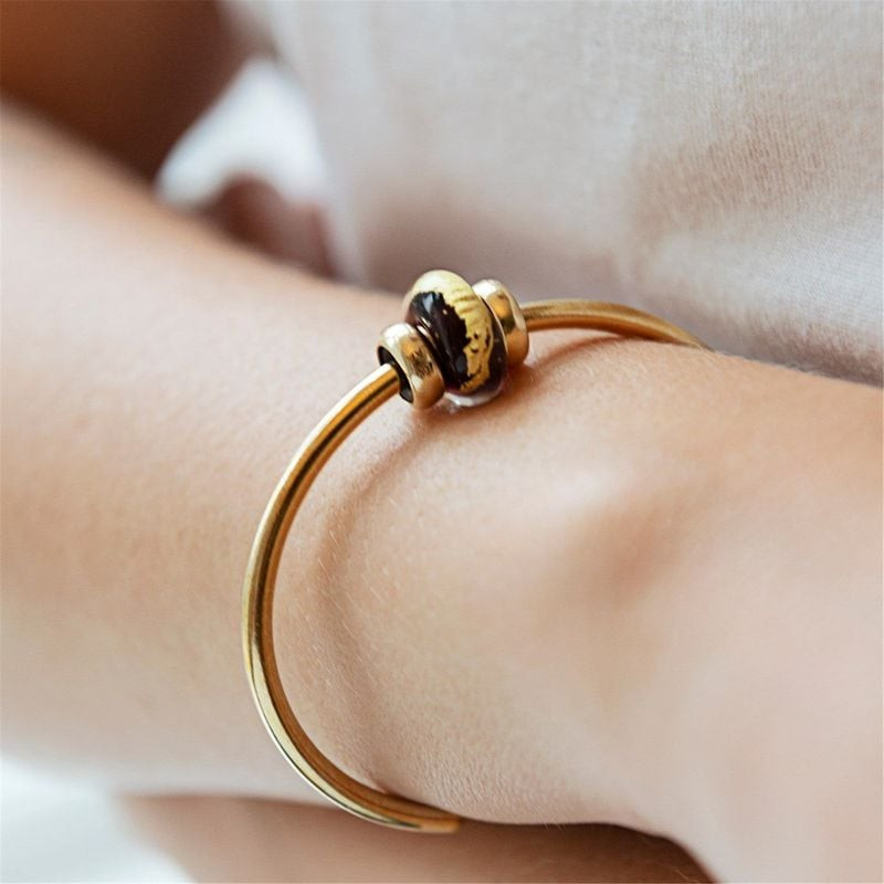 Perle Trollbeads Troisième œil en verre et or sur un jonc doré porté au poignet d'une femme, gros pl