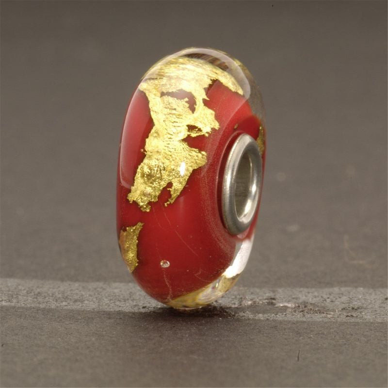 Bille Trollbeads Chakra racine en verre posée sur surface grise, détail de la feuille d'or