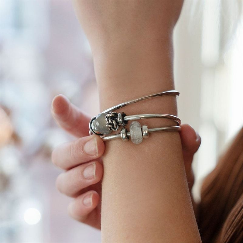 Poignet d'une femme portant un jonc et un bracelet Trollbeads en argent avec la breloque en verre Lu
