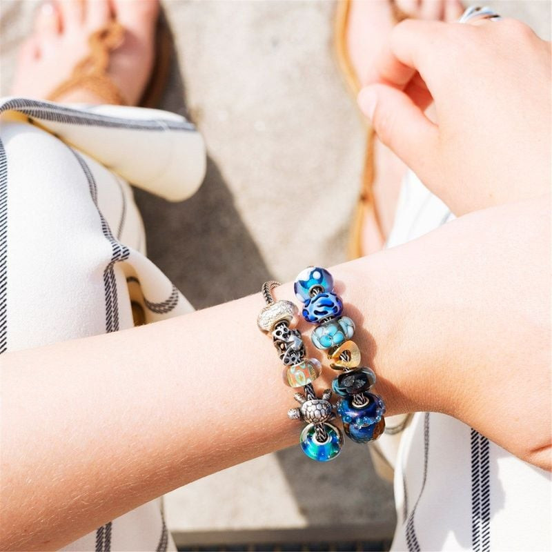 Poignet avec bracelet Trollbeads argent et perle de verre guépard bleu parmi des breloques colorées,