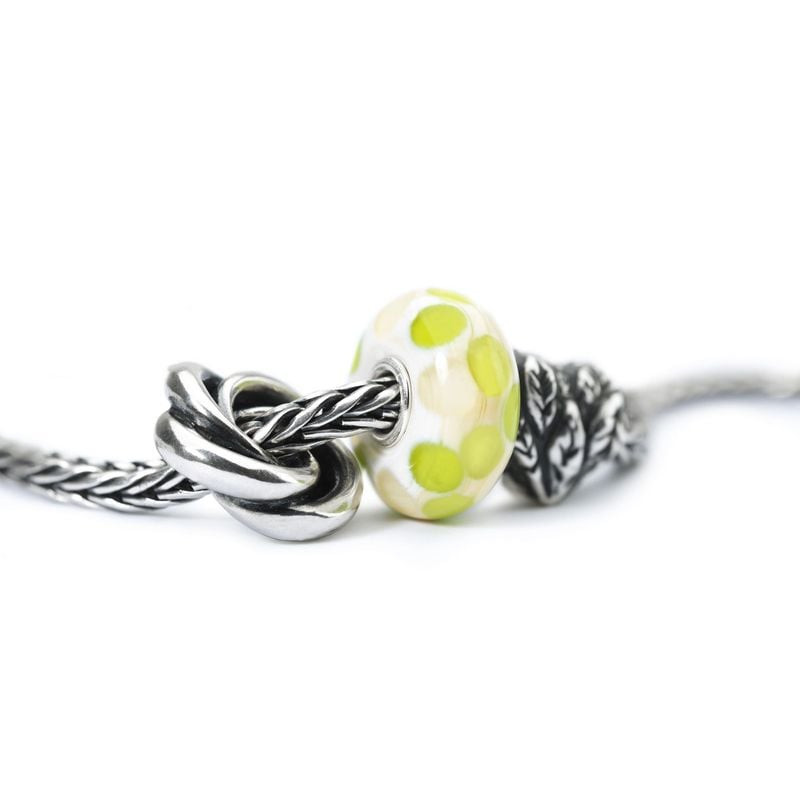 Perle Trollbeads Sommeil présentée sur une chaîne argentée près d'un détail noué, arrière-plan douce
