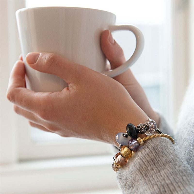 Poignet portant un bracelet Trollbeads avec la perle Bulles aux ondulations violettes et des charms,