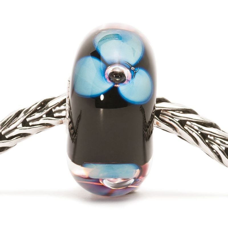 Perle en verre bleu Trollbeads Fleur de l'aurore enfilée sur un bracelet chaîne en argent, vue d'amb