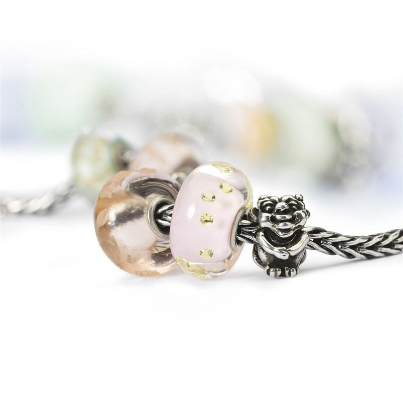 Perle en verre rose Pureté Fragile sur bracelet Trollbeads avec breloques pêche et vert, fond flou d