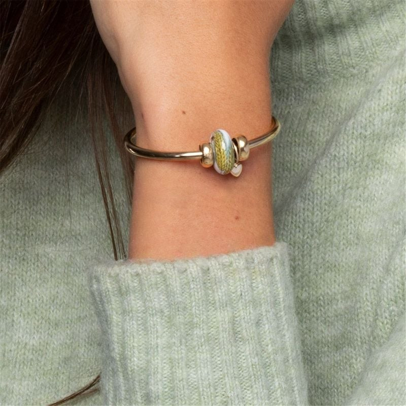 Perle en porcelaine Graines Généreuses portée sur un jonc Trollbeads doré avec une manche en tricot 