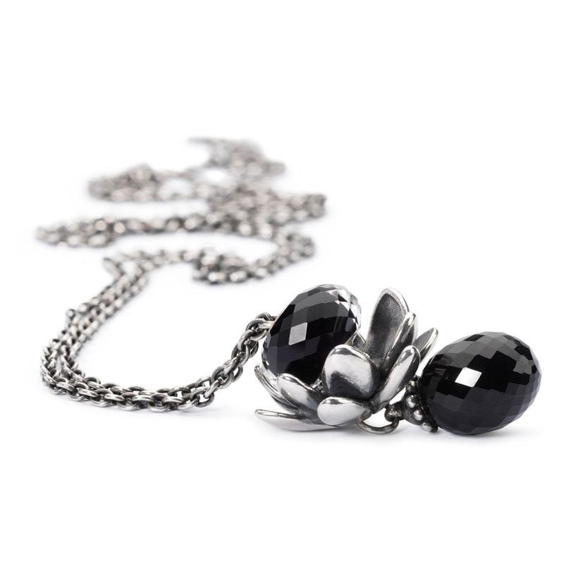 Gros plan sur une perle d'onyx noir facettée sertie dans une fleur de lotus en argent sur une chaîne