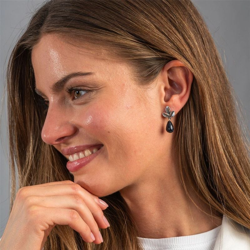 Modèle souriante, main au menton, puces d'oreilles Trollbeads Feuilles de Force argent et goutte de 
