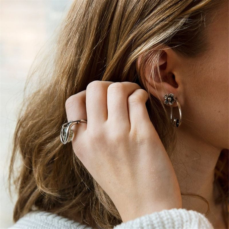 Femme aux cheveux ondulés les ramenant derrière l'oreille, montrant la boucle d'oreille Fleur Réjoui