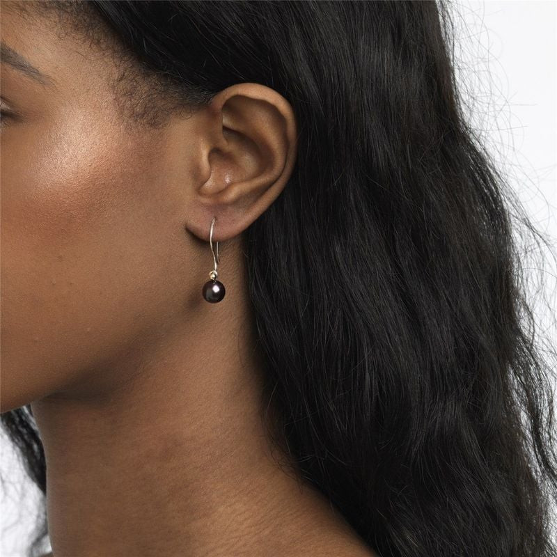 Une femme portant une boucle d'oreille Trollbeads Goutte ronde de perle plume de paon à l'oreille ga