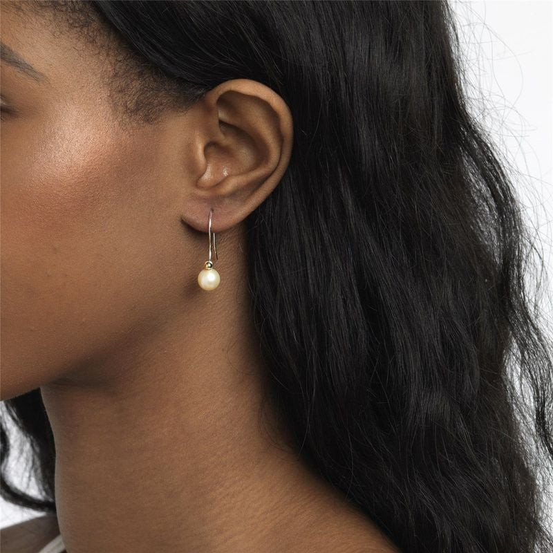 Gros plan d'un mannequin à la peau foncée portant une boucle d'oreille goutte perle blanche Trollbea