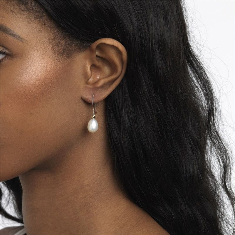 Gros plan sur une oreille féminine portant une boucle d'oreille Trollbeads goutte en perle blanche o