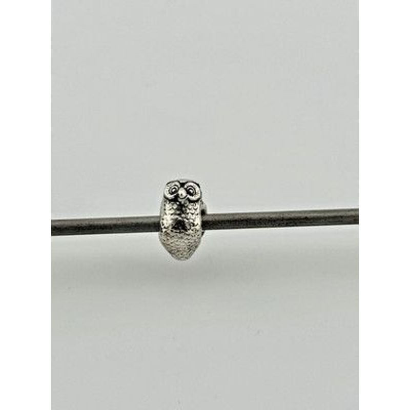Perle Trollbeads Hibou en argent 925, taille réelle, enfilée sur un cordon sur fond gris uni
