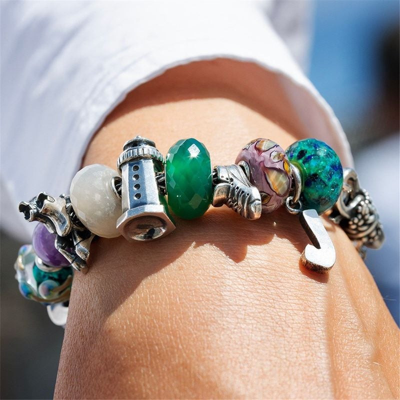 Une main portant un bracelet Trollbeads avec la perle Foulées Vitales, associé à une chemise blanche