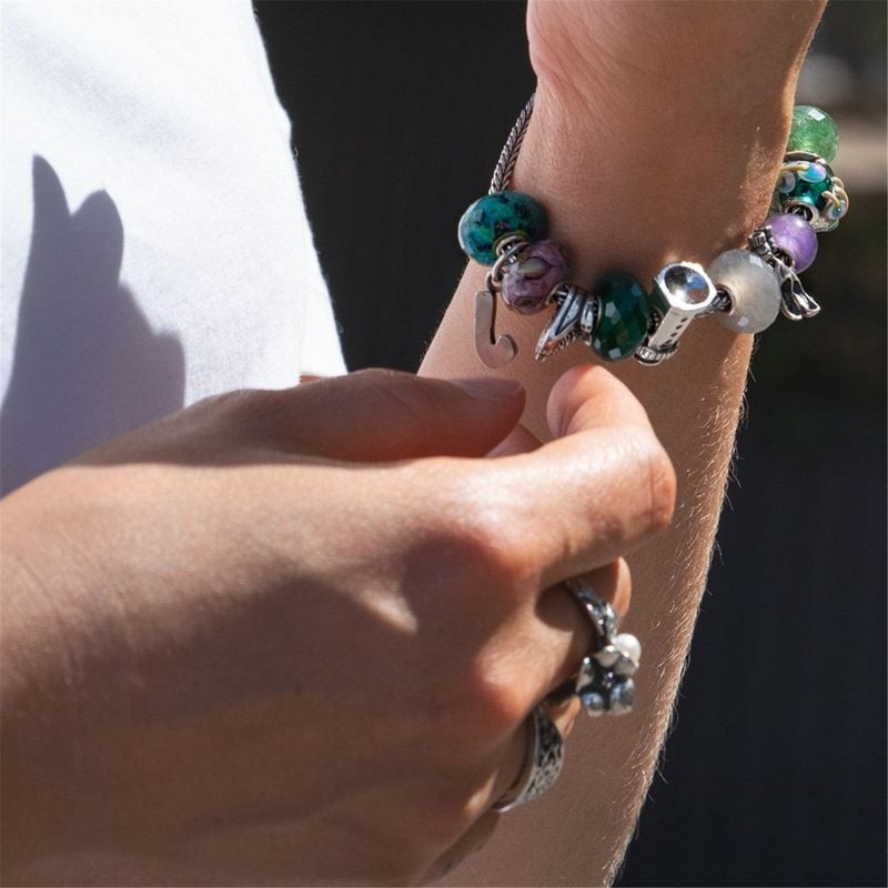 Gros plan d'une main ajustant un bracelet Trollbeads avec la perle Foulées Vitales et d'autres perle