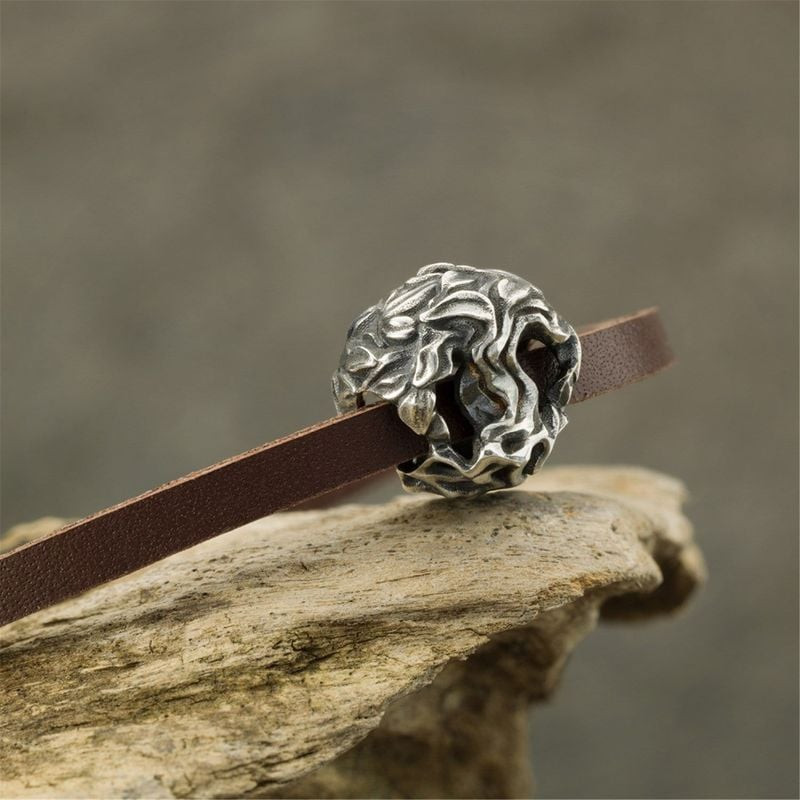 Perle TROLLBEADS Arbre de la Vie en argent sur un bracelet en cuir marron, posée sur du bois flotté