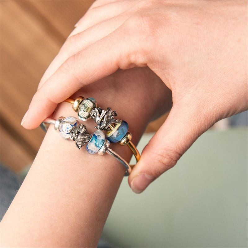 Une main portant un bracelet orné de la perle de charme TROLLBEADS ALGUE ARGENTÉ et d'autres perles 