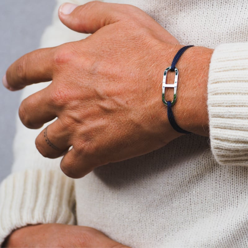 Gros plan d'une main portant le bracelet Gaby en argent rhodié sur un cordon bleu marine avec un pul