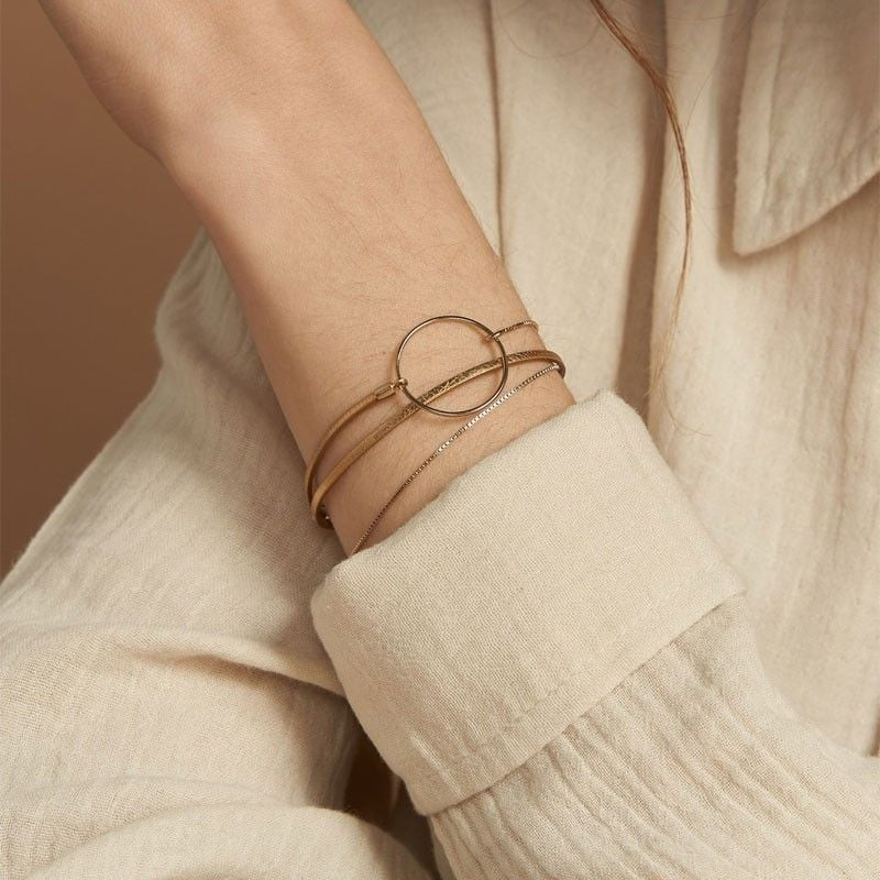 Bracelet Nolah porté au poignet avec une chemise en lin beige, anneau doré, chaîne et lien en cuir